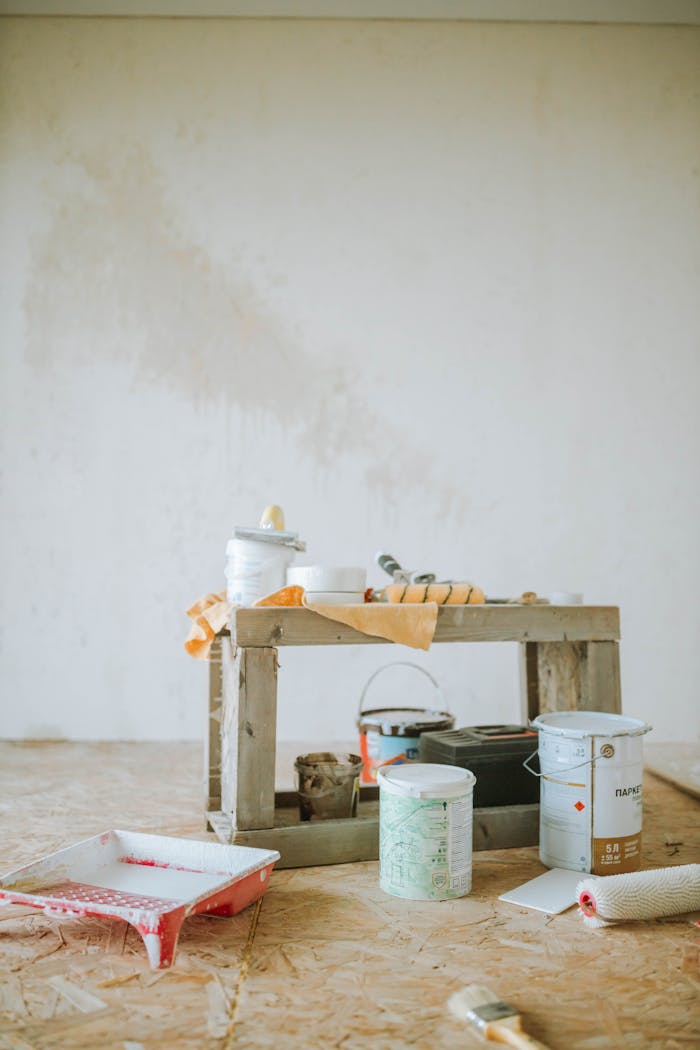 A collection of paint supplies for home renovation placed on the floor indoors, ready for wall painting.
